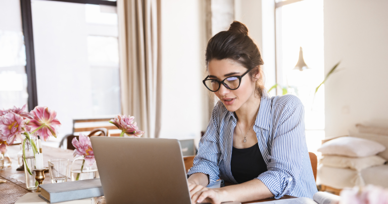 Woman with glasses working at a laptop with flowers on the desk