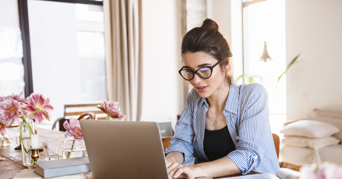 Woman with glasses working at a laptop with flowers on the desk